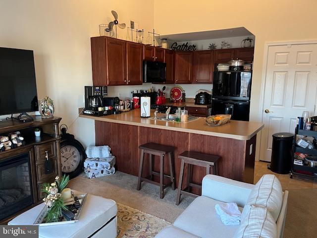 kitchen with black appliances, a kitchen bar, light colored carpet, and kitchen peninsula