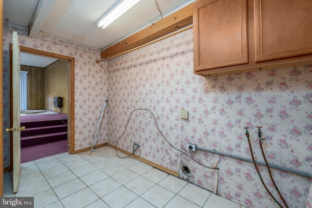 clothes washing area featuring cabinets, light tile patterned floors, and a textured ceiling