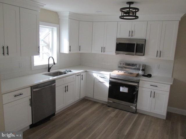 kitchen with appliances with stainless steel finishes, light wood-type flooring, a sink, and tasteful backsplash