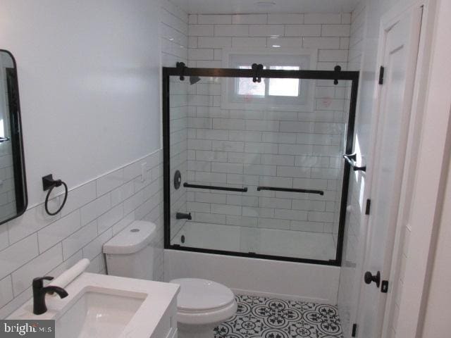 bathroom with enclosed tub / shower combo, tile patterned flooring, toilet, vanity, and tile walls