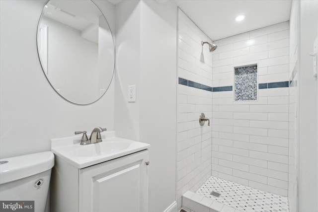 bathroom with a tile shower, vanity, and toilet