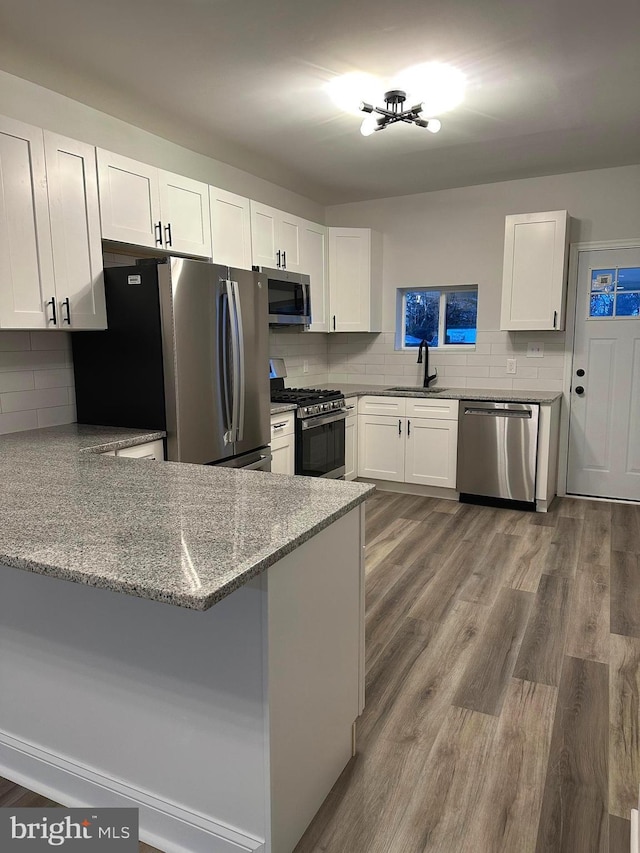 kitchen with kitchen peninsula, appliances with stainless steel finishes, white cabinetry, and wood-type flooring