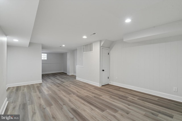 basement with light wood-type flooring and wooden walls