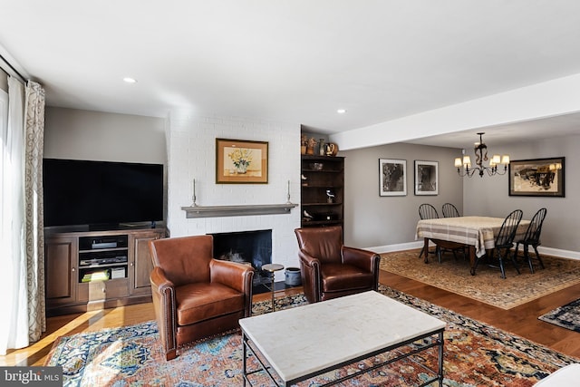 living room featuring a brick fireplace, light wood-type flooring, and an inviting chandelier