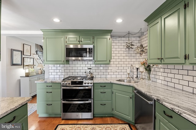 kitchen featuring green cabinets, sink, decorative backsplash, light wood-type flooring, and appliances with stainless steel finishes