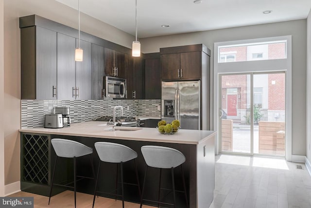 kitchen featuring stainless steel appliances, backsplash, kitchen peninsula, decorative light fixtures, and dark brown cabinets