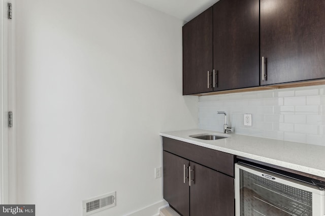 kitchen featuring decorative backsplash, dark brown cabinetry, wine cooler, and sink