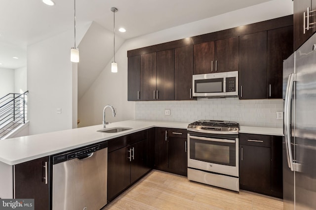 kitchen featuring kitchen peninsula, appliances with stainless steel finishes, light wood-type flooring, sink, and hanging light fixtures