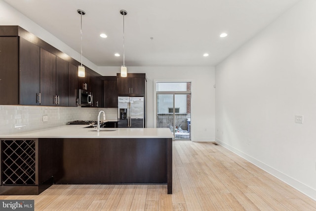 kitchen with hanging light fixtures, light wood-type flooring, dark brown cabinets, kitchen peninsula, and stainless steel appliances