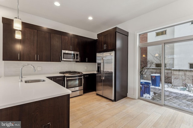 kitchen featuring dark brown cabinets, stainless steel appliances, sink, light hardwood / wood-style floors, and hanging light fixtures