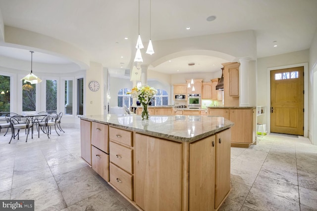 kitchen featuring a center island, light brown cabinets, light stone countertops, appliances with stainless steel finishes, and decorative light fixtures