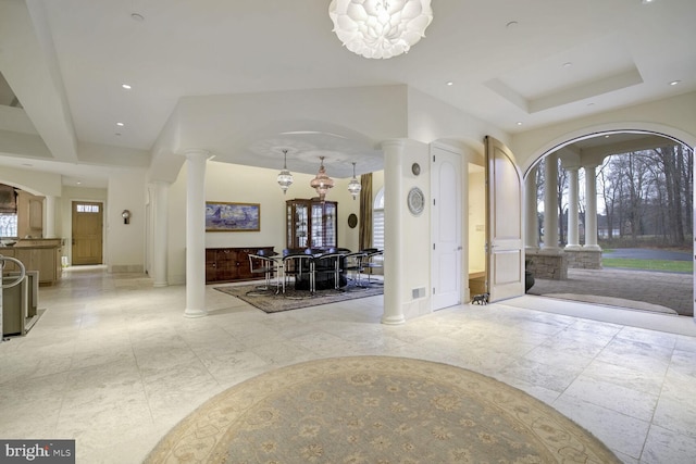 entryway featuring a raised ceiling, ornate columns, and a chandelier