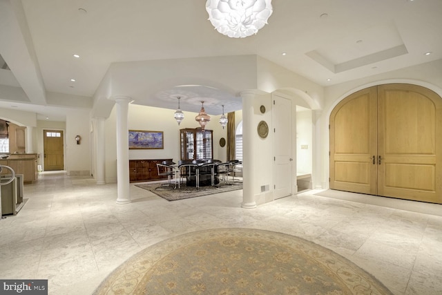 foyer with a raised ceiling, ornate columns, and a chandelier