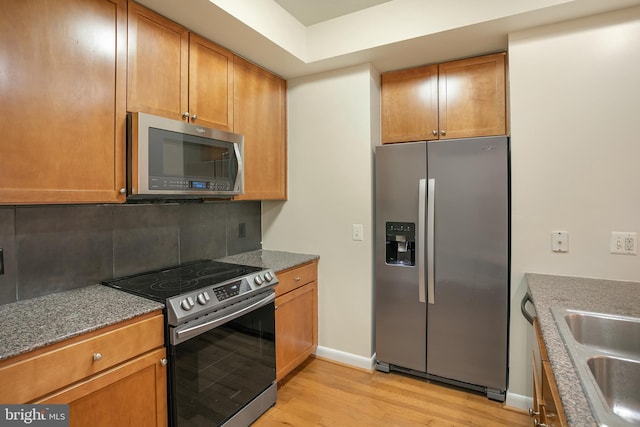 kitchen with tasteful backsplash, sink, light hardwood / wood-style floors, and appliances with stainless steel finishes