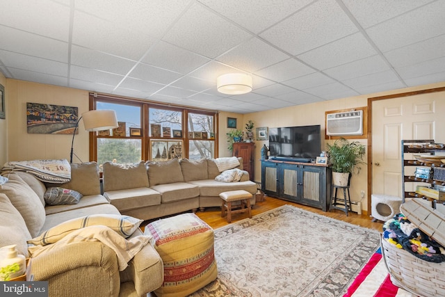 living area with a paneled ceiling, an AC wall unit, and wood finished floors