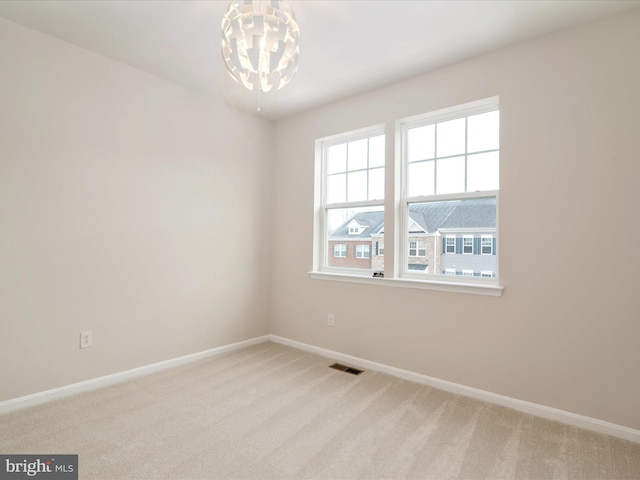 unfurnished room featuring a chandelier and light carpet