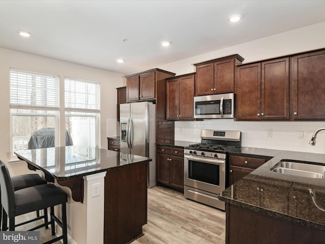 kitchen featuring sink, a center island, dark stone counters, stainless steel appliances, and backsplash