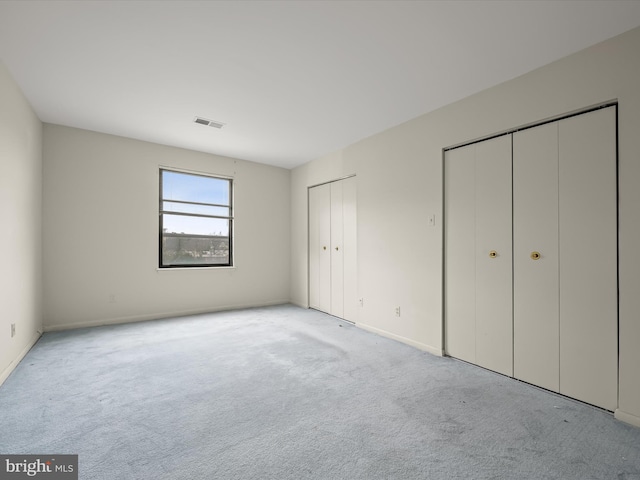 unfurnished bedroom with light colored carpet and multiple closets