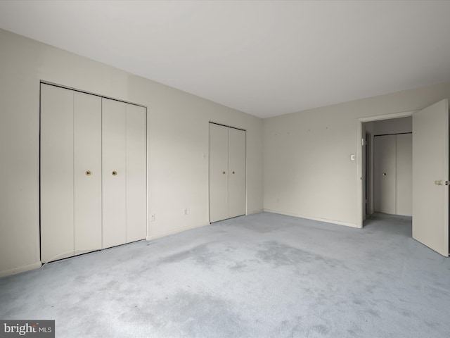 unfurnished bedroom featuring multiple closets and light colored carpet