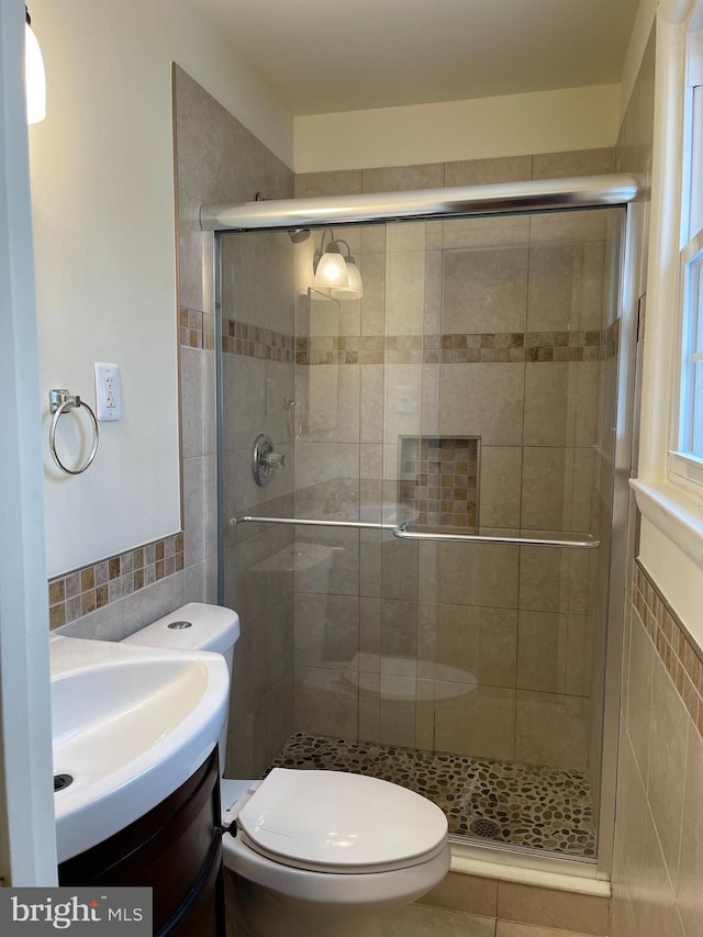 bathroom featuring toilet, tile walls, a shower with shower door, and vanity