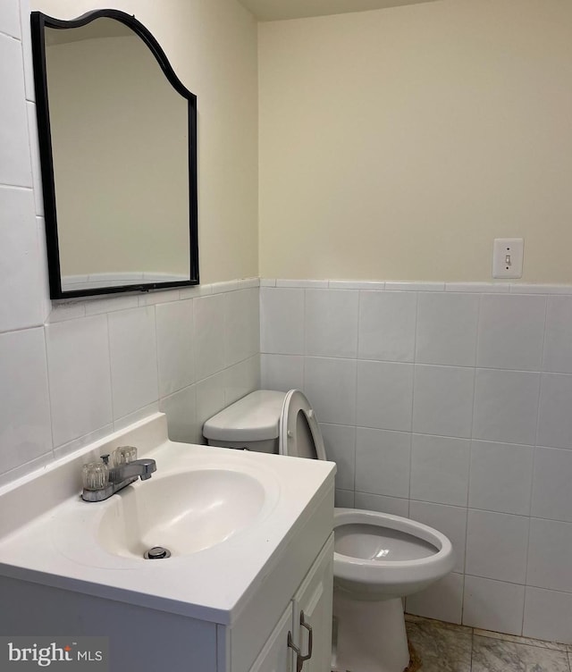 bathroom with toilet, vanity, and tile walls