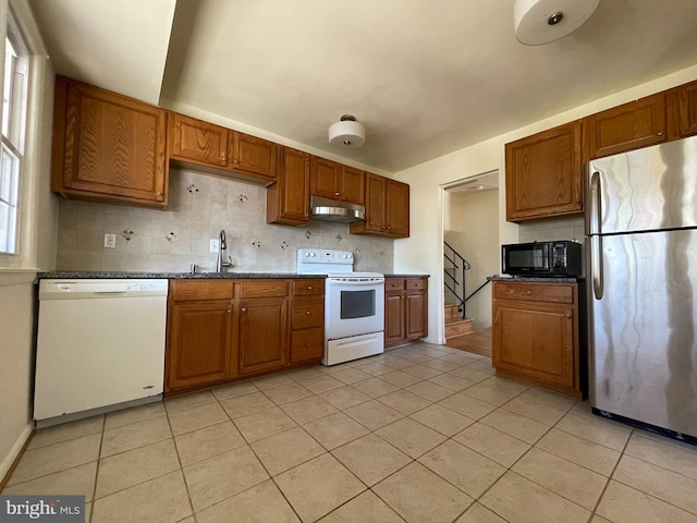 kitchen with decorative backsplash, white appliances, light tile patterned flooring, dark stone countertops, and sink