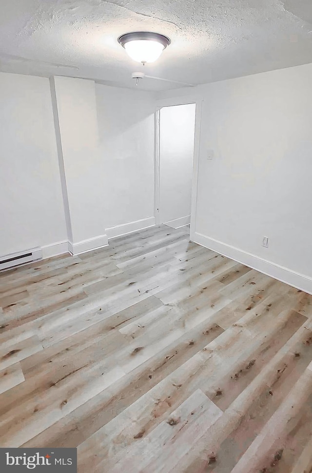 unfurnished room with a baseboard radiator, a textured ceiling, and light wood-type flooring