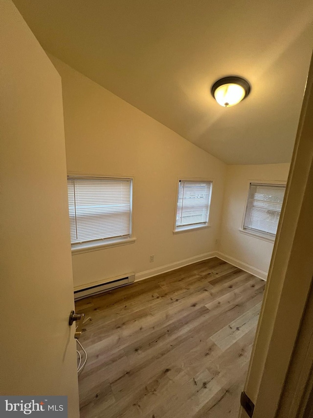 empty room featuring a baseboard radiator, vaulted ceiling, and light wood-type flooring