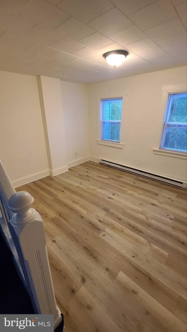 spare room featuring baseboard heating and light hardwood / wood-style flooring