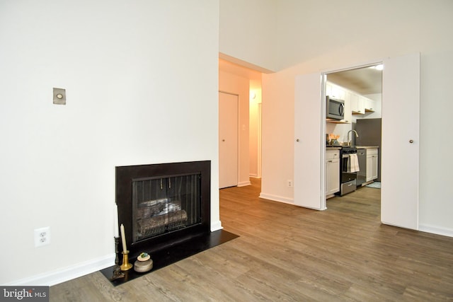 living area featuring a fireplace with flush hearth, wood finished floors, and baseboards