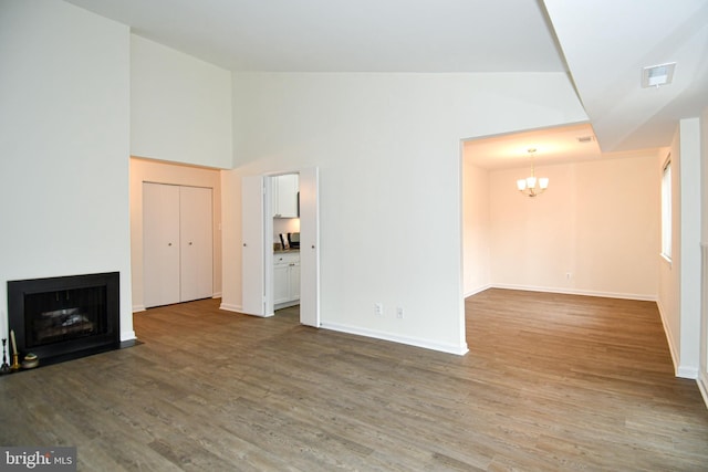 unfurnished living room featuring wood finished floors, an inviting chandelier, a fireplace with flush hearth, and baseboards