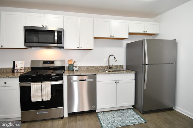 kitchen featuring stone counters, stainless steel appliances, wood finished floors, a sink, and white cabinets