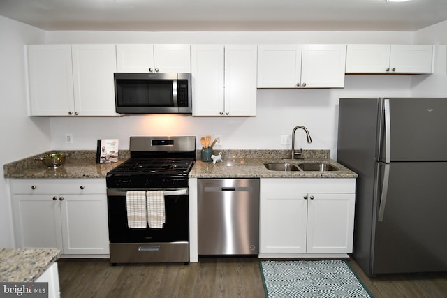 kitchen featuring stone counters, dark wood-style flooring, stainless steel appliances, white cabinets, and a sink