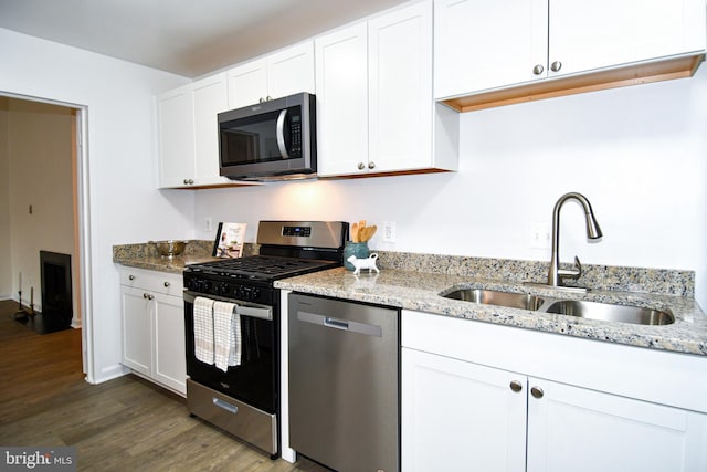 kitchen featuring appliances with stainless steel finishes, a sink, light stone counters, and white cabinets