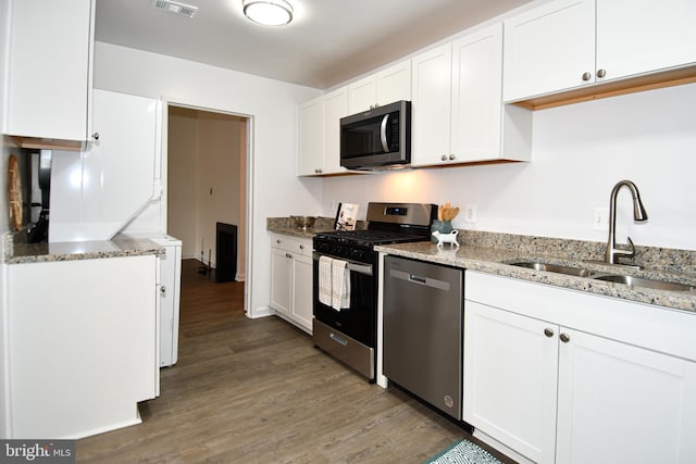 kitchen with light stone counters, stainless steel appliances, white cabinets, a sink, and wood finished floors