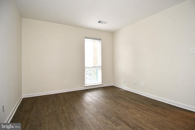 spare room featuring dark wood-style floors, visible vents, and baseboards