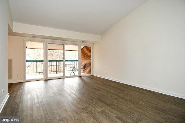 spare room featuring a brick fireplace, dark wood finished floors, and baseboards