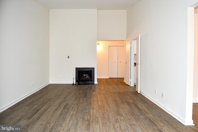 unfurnished living room featuring a fireplace with flush hearth, a high ceiling, baseboards, and dark wood-style flooring