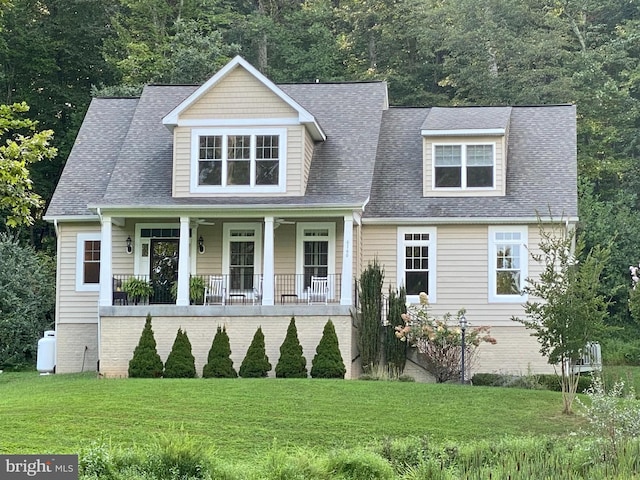 view of front of property with covered porch, a front lawn, roof with shingles, and a view of trees