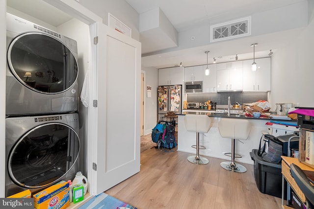 clothes washing area with stacked washer and dryer, light hardwood / wood-style floors, and sink