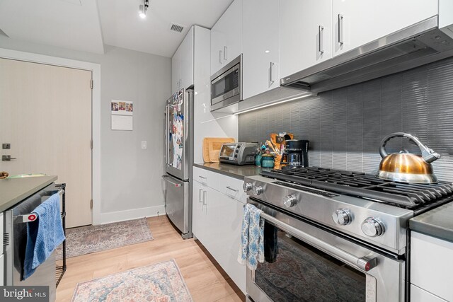 kitchen with white cabinets, appliances with stainless steel finishes, backsplash, and light hardwood / wood-style floors