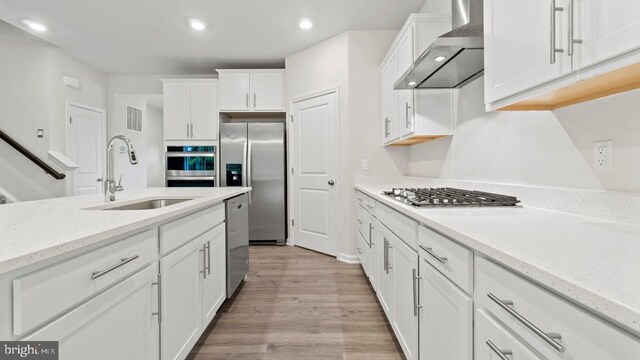 kitchen featuring stainless steel appliances, sink, wall chimney range hood, light hardwood / wood-style floors, and white cabinetry