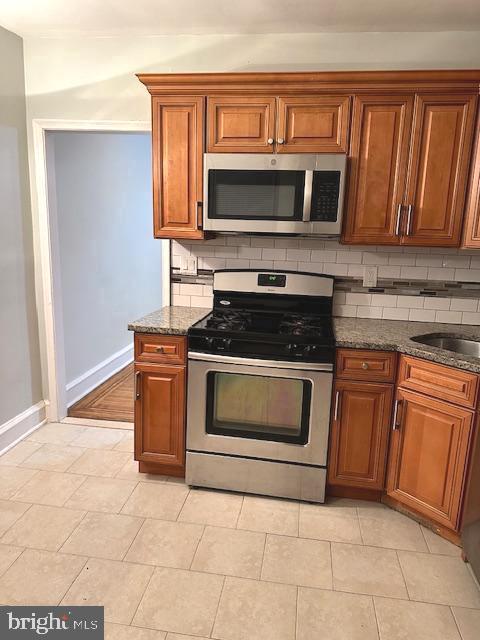 kitchen featuring backsplash, sink, dark stone counters, and stainless steel appliances