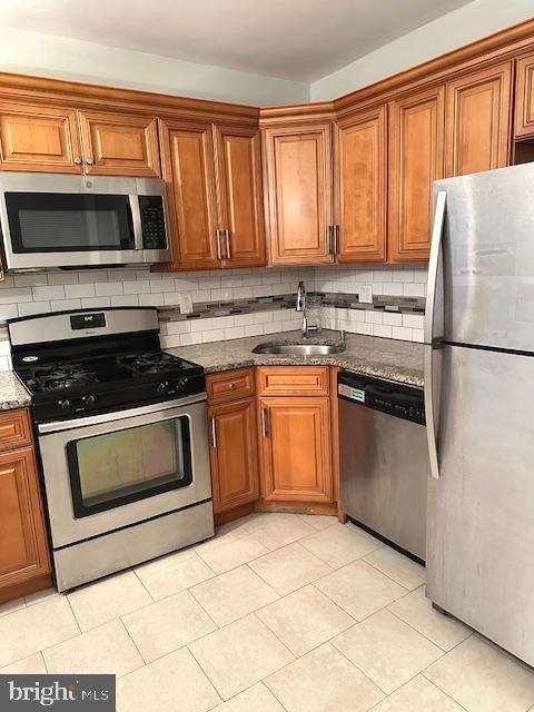 kitchen with sink, stainless steel appliances, dark stone countertops, decorative backsplash, and light tile patterned flooring