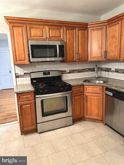 kitchen with stainless steel appliances, tasteful backsplash, dark stone countertops, and sink