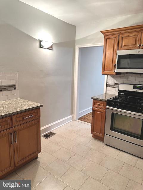 kitchen featuring backsplash, light stone countertops, light tile patterned floors, and stainless steel appliances