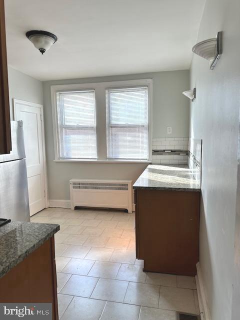 kitchen with dark stone countertops, stainless steel fridge, radiator heating unit, and plenty of natural light