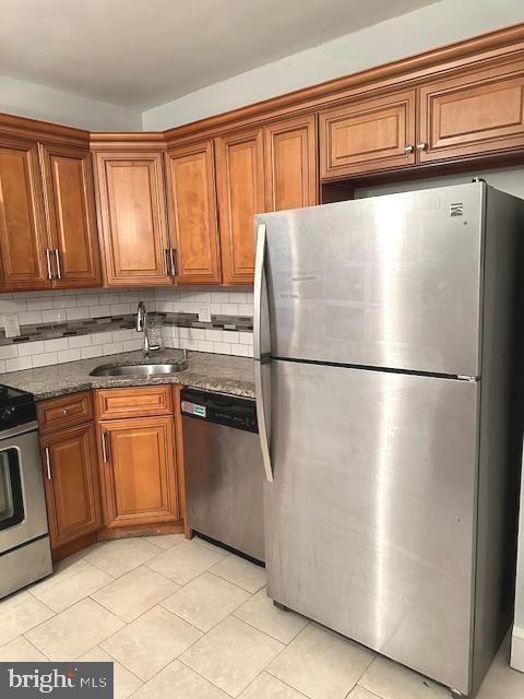 kitchen with sink, dark stone countertops, light tile patterned floors, appliances with stainless steel finishes, and tasteful backsplash