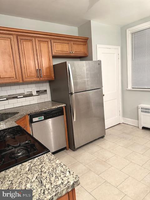 kitchen with backsplash, stainless steel appliances, sink, stone countertops, and radiator heating unit