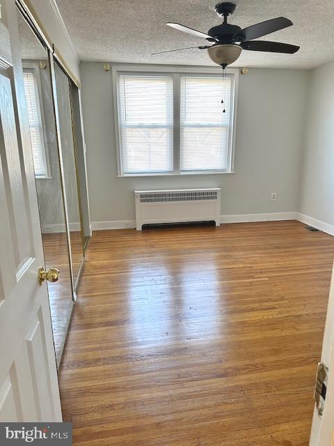 unfurnished bedroom featuring radiator, ceiling fan, a textured ceiling, and light wood-type flooring